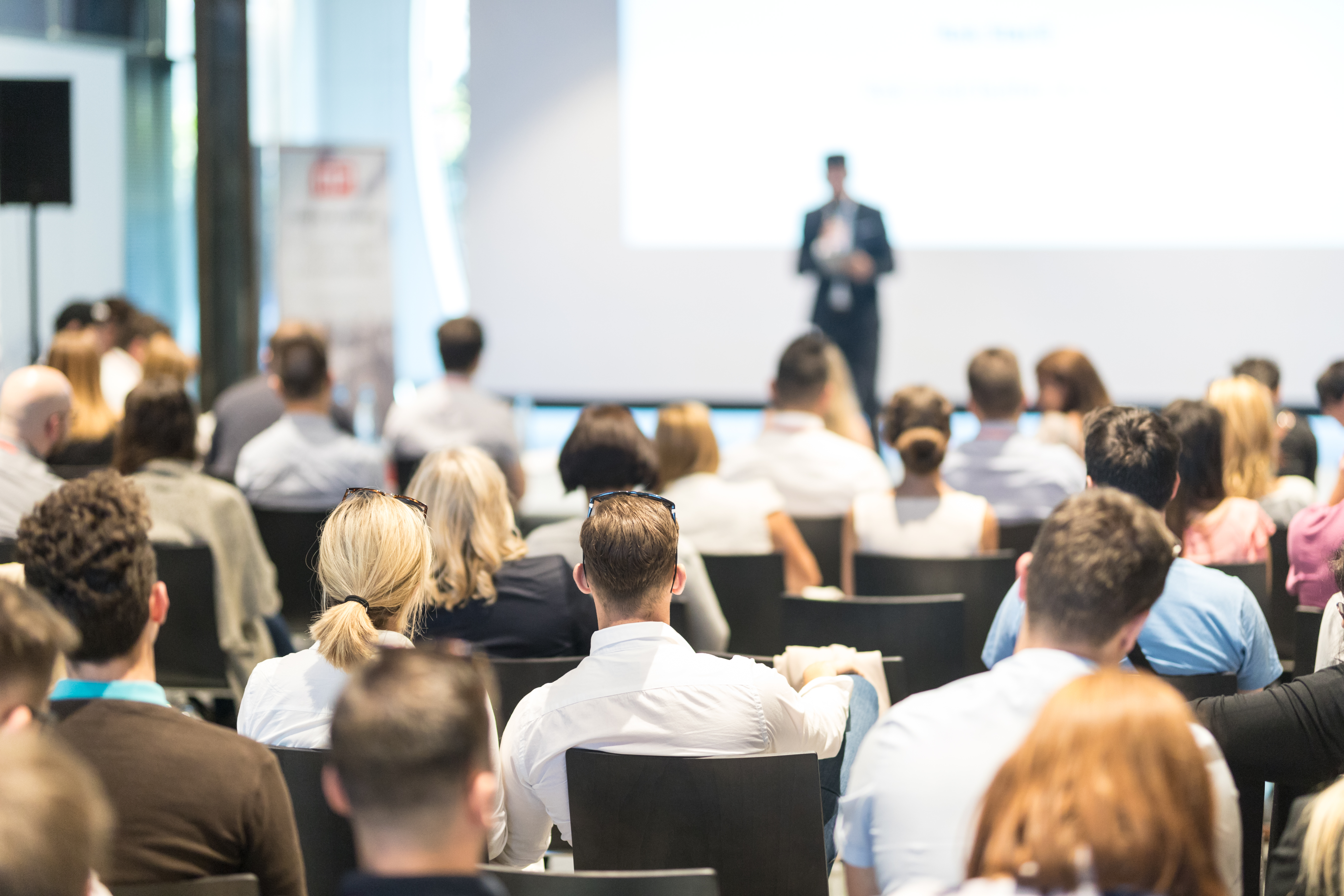 Conférence professionnelle: public assis écoute un orateur sur scène lors d’un séminaire.